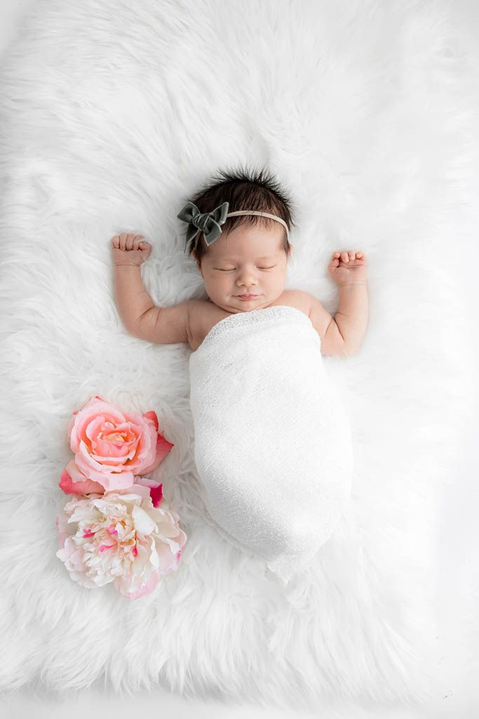 Sleeping newborn baby girl wrapped in white with pink roses on fluffy white fur.