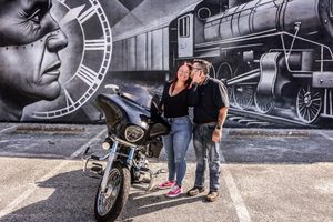 Couple kissing beside a motorcycle in front of a colorful street mural.