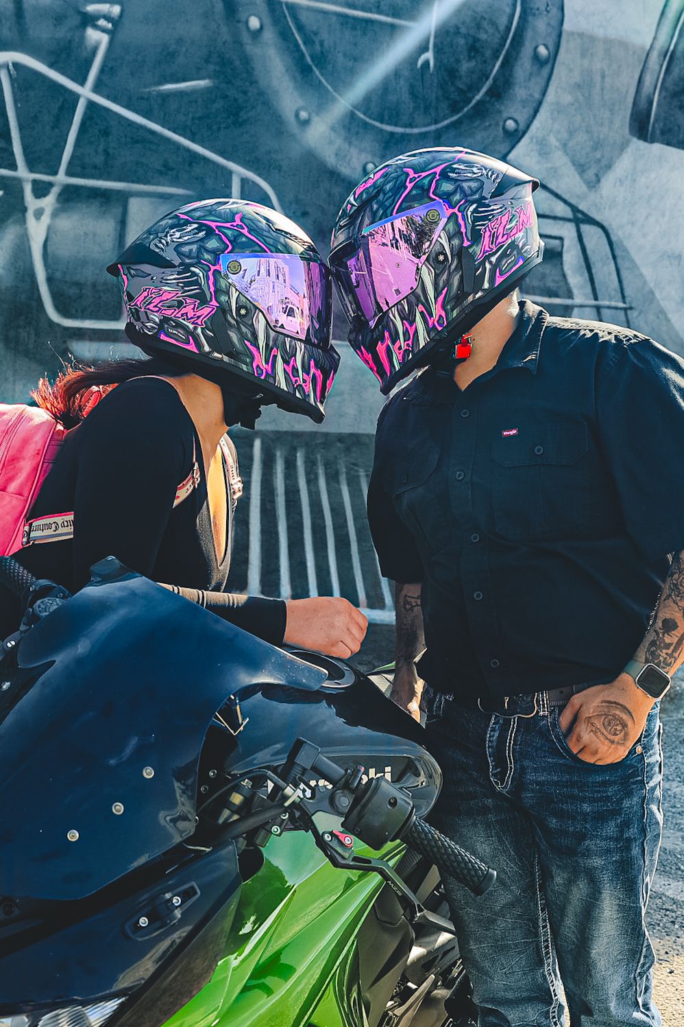 A couple wearing matching purple and black helmets share a kiss near a green Kawasaki motorcycle.
