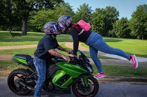 Woman in pink sneakers leaning over a green Kawasaki sport bike in a park.