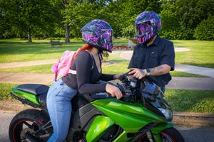 Couple in matching purple helmets sitting on a green Kawasaki sport bike in a park.
