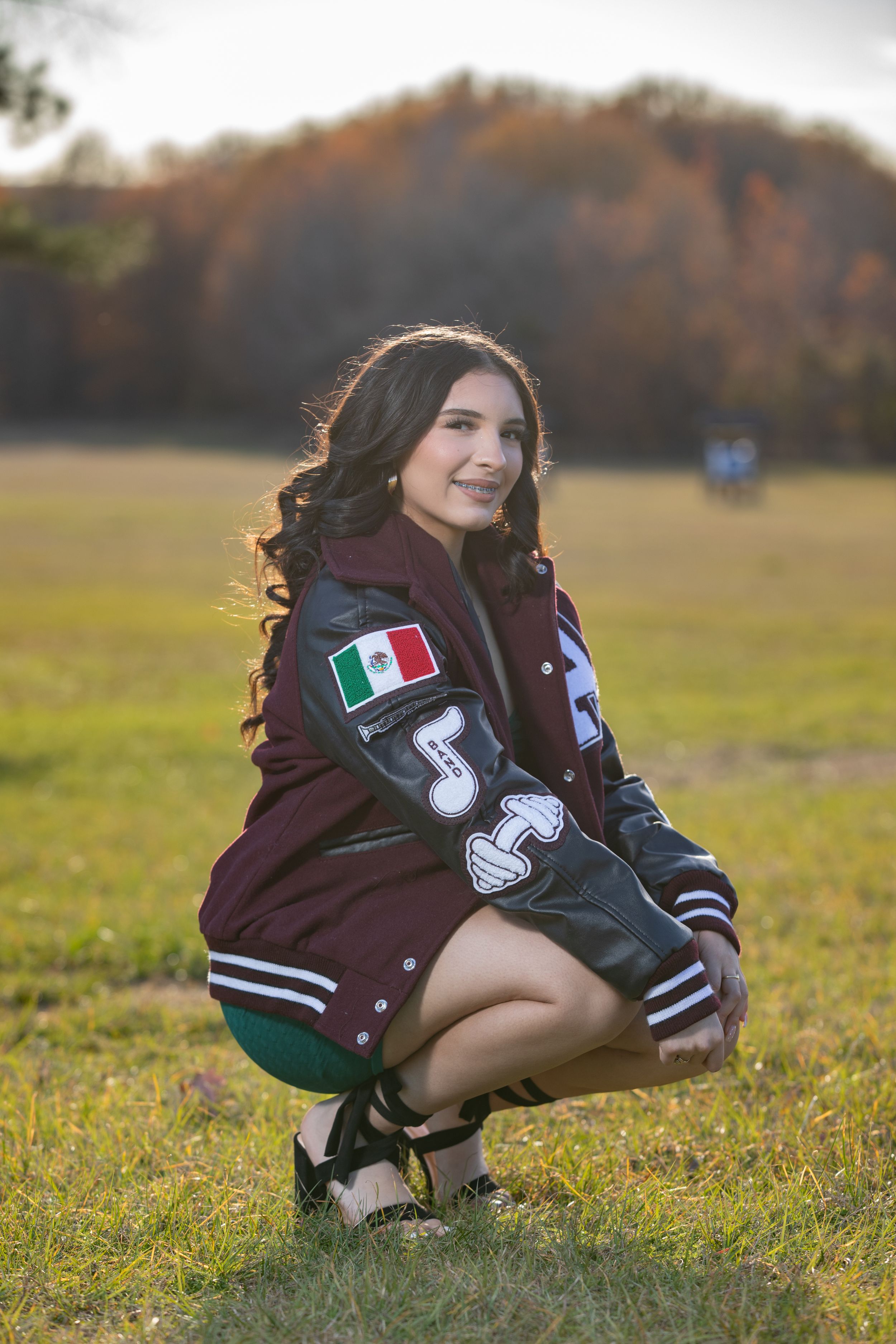 Letterman jacket photo session in grassy field during autumn sunset.