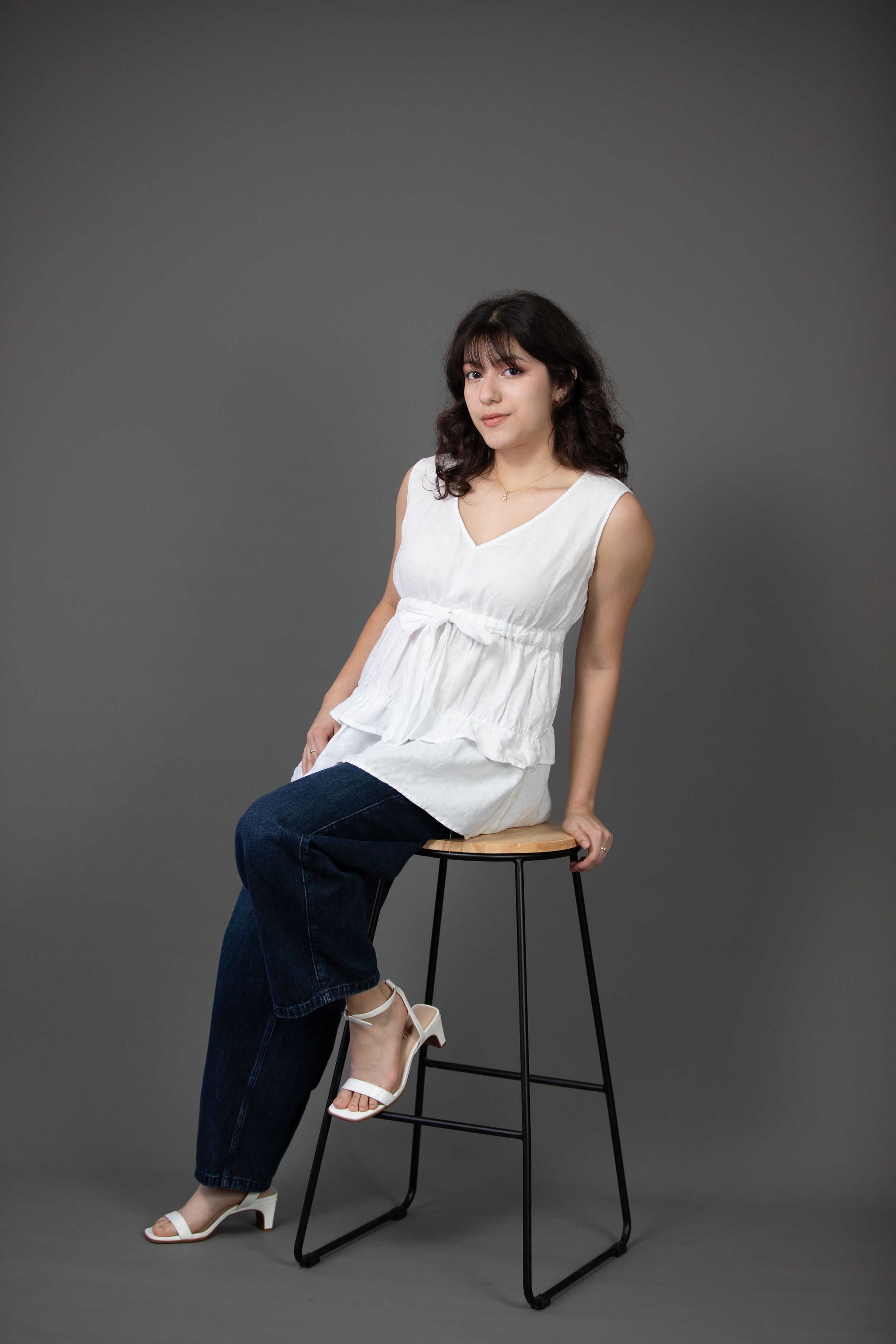 Studio portrait featuring white tiered top and jeans on modern black barstool.