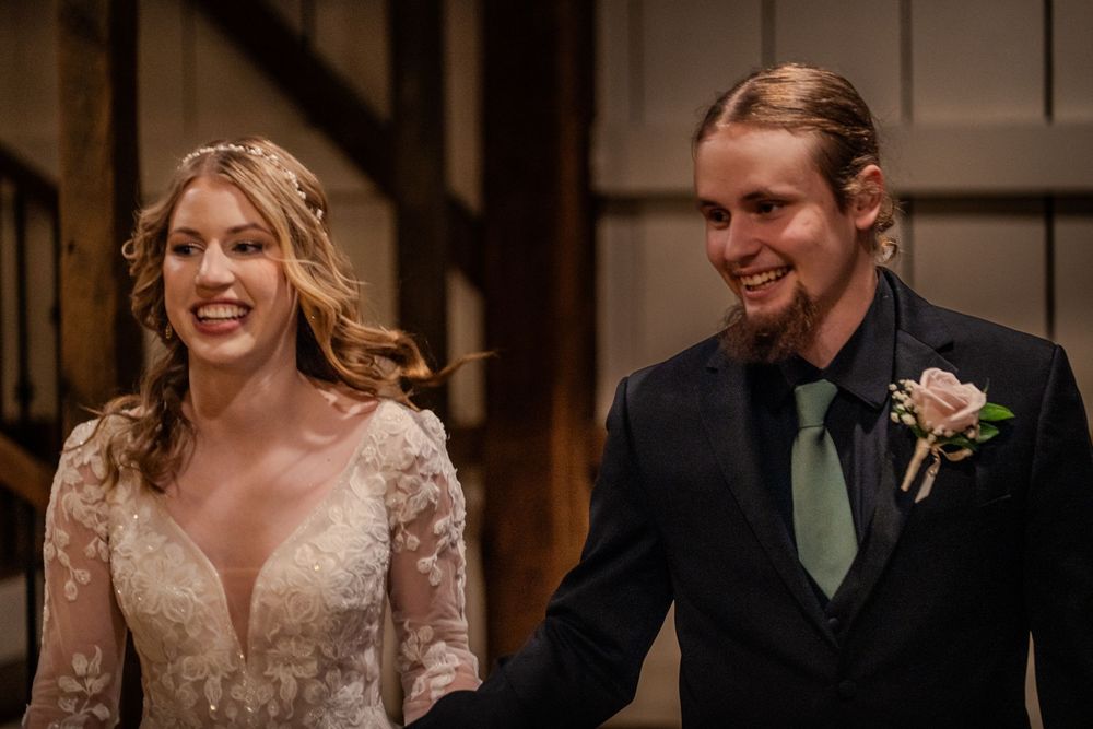 Smiling bride in lace gown and groom in dark suit with green tie and pink boutonniere at wedding ceremony.