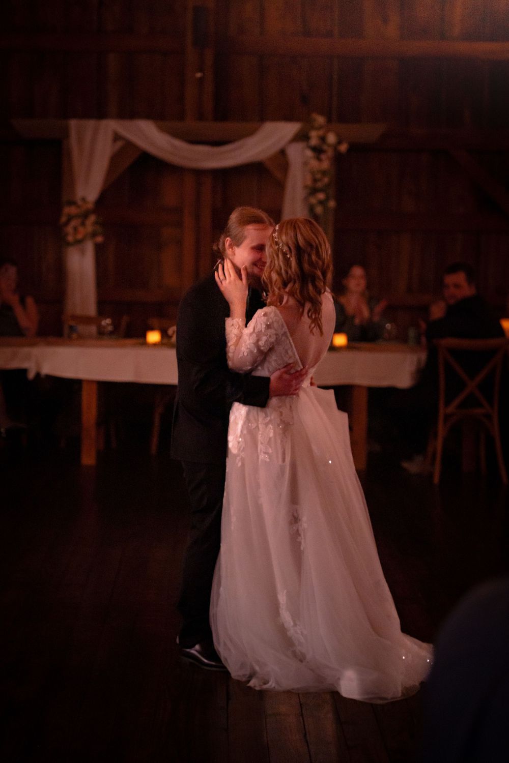 Bride and groom share their first dance in a warmly lit rustic barn wedding venue.