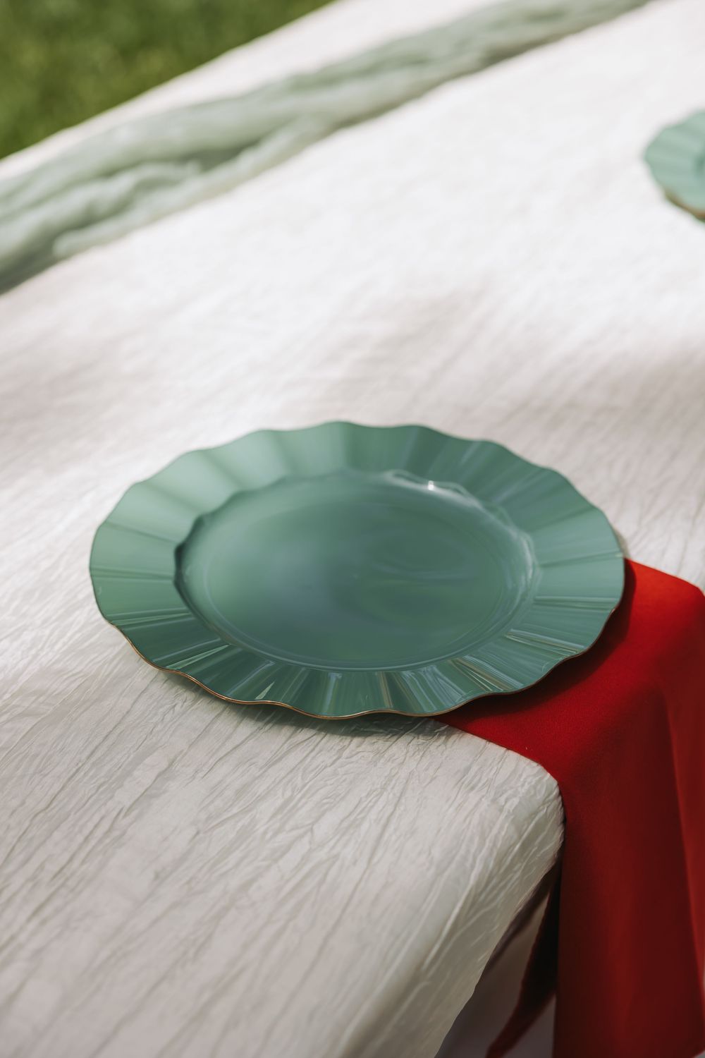 Green scalloped edge plate on red napkin and white textured tablecloth for elegant outdoor dining.