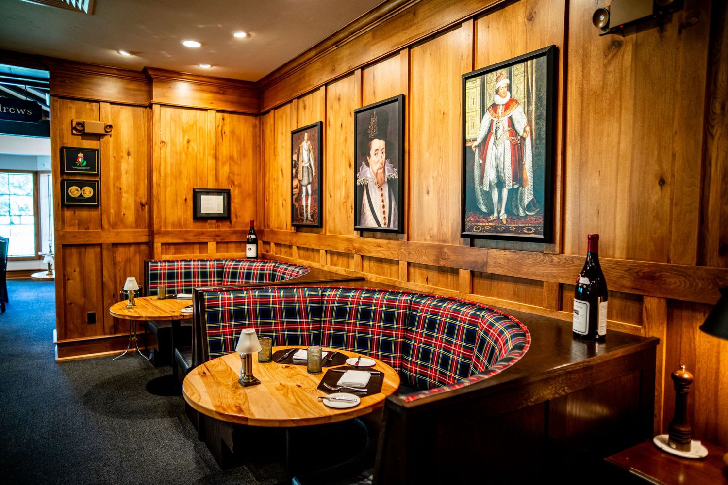 Cozy restaurant booth with red tartan upholstery, wood-paneled walls, royal portrait paintings, and round wooden tables.