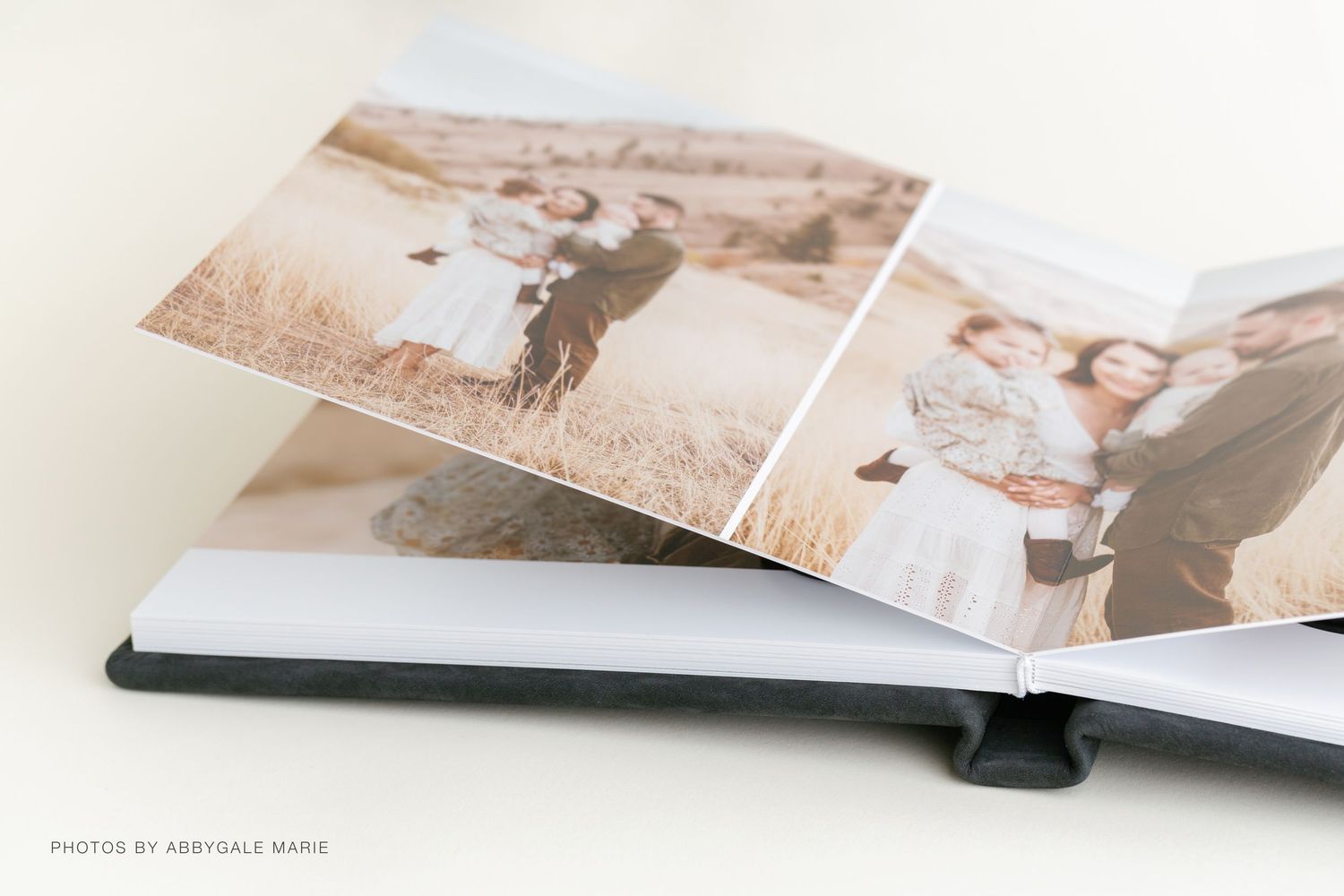 Two elegant hardcover wedding photo albums stacked, one open showing ceremony photos, in navy blue linen and white covers.