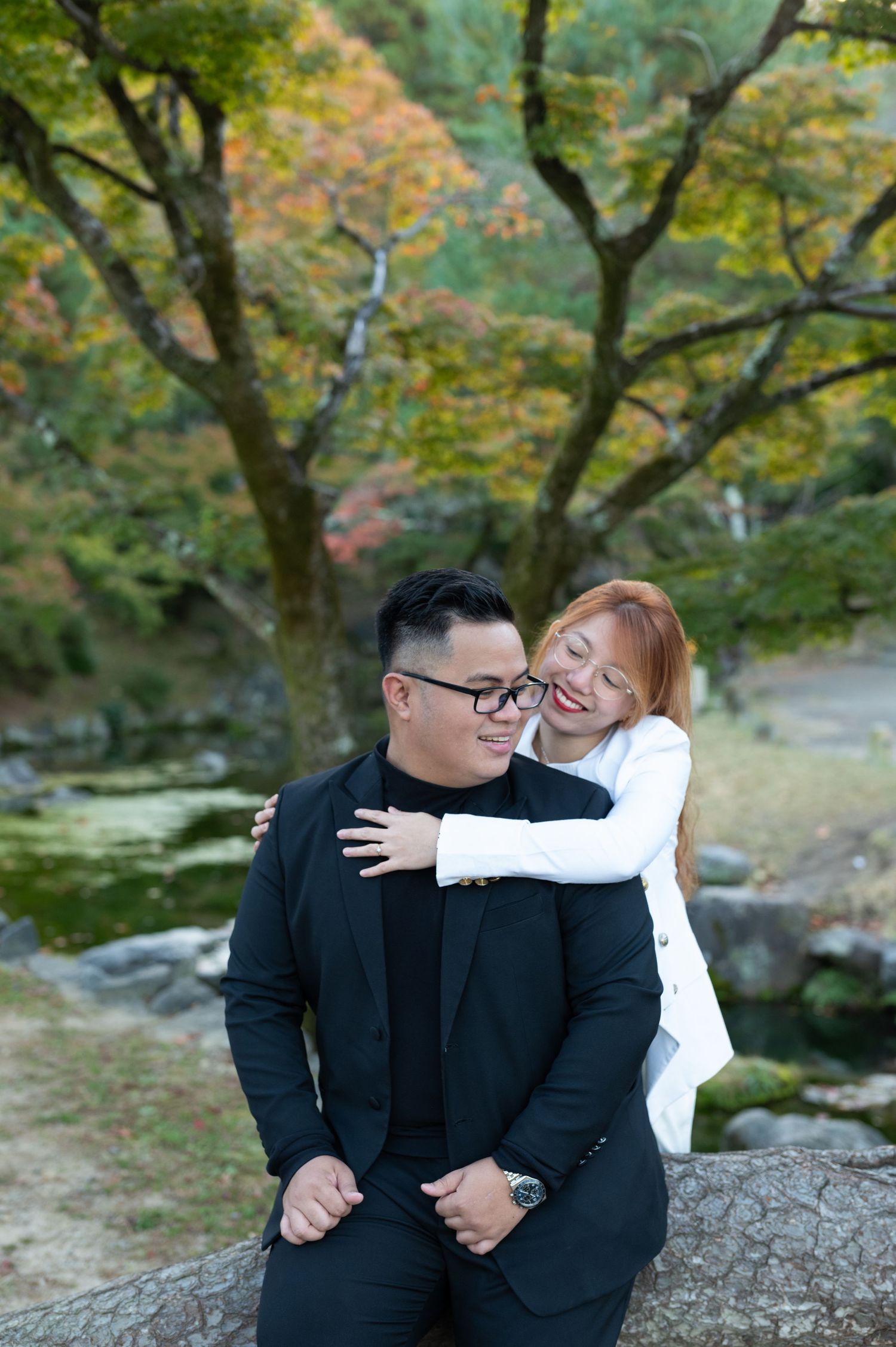Smiling couple embracing outdoors with colorful autumn trees in the background.