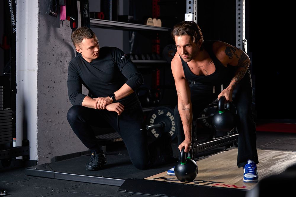 A personal trainer coaches a woman lifting a kettlebell in a modern gym setting.