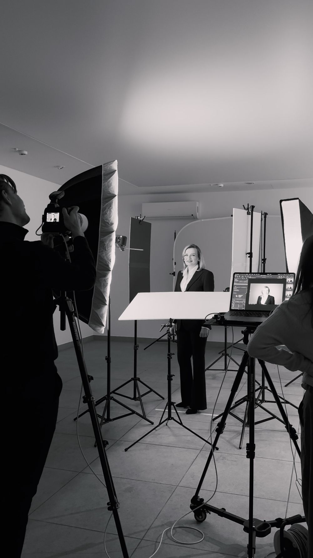Black and white photo of a professional video production studio shoot with lighting equipment, camera operator, and subject posing.