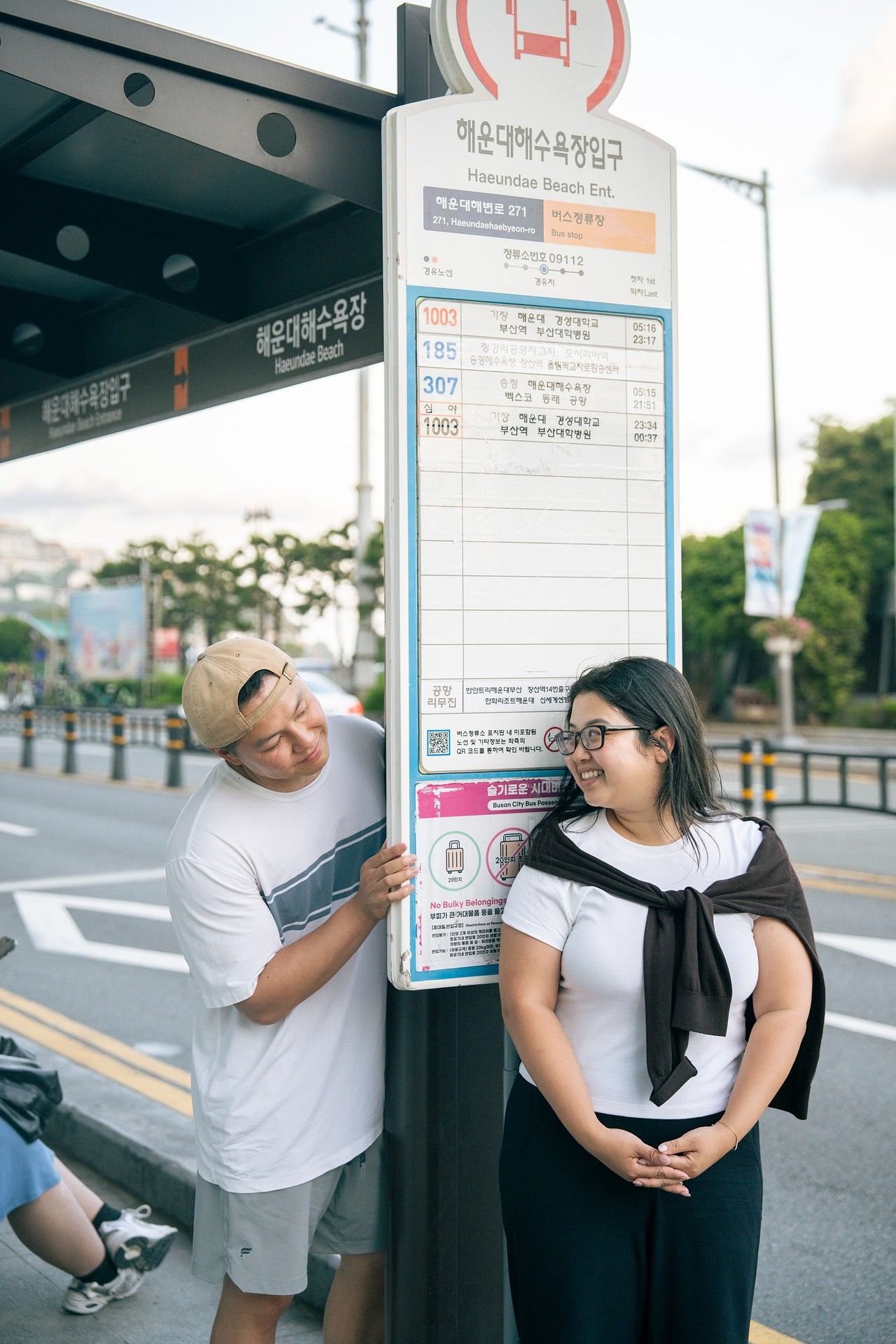 Couple smiling at a bus stop sign at Haeundae Beach Entrance in Busan, South Korea.