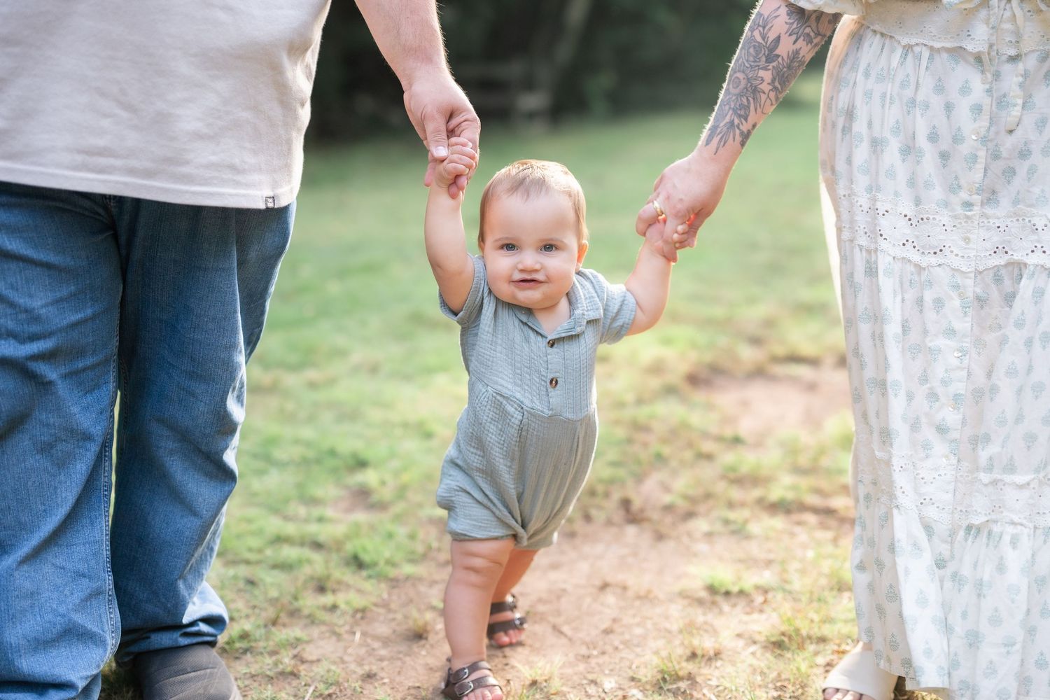 Baby taking steps while holding mom and dads hands smiling