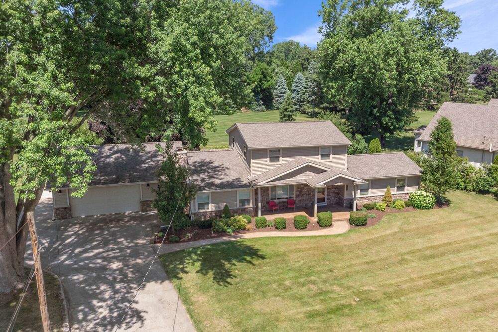 Aerial view of two-story home with attached garage, red porch, and expansive green lawn.