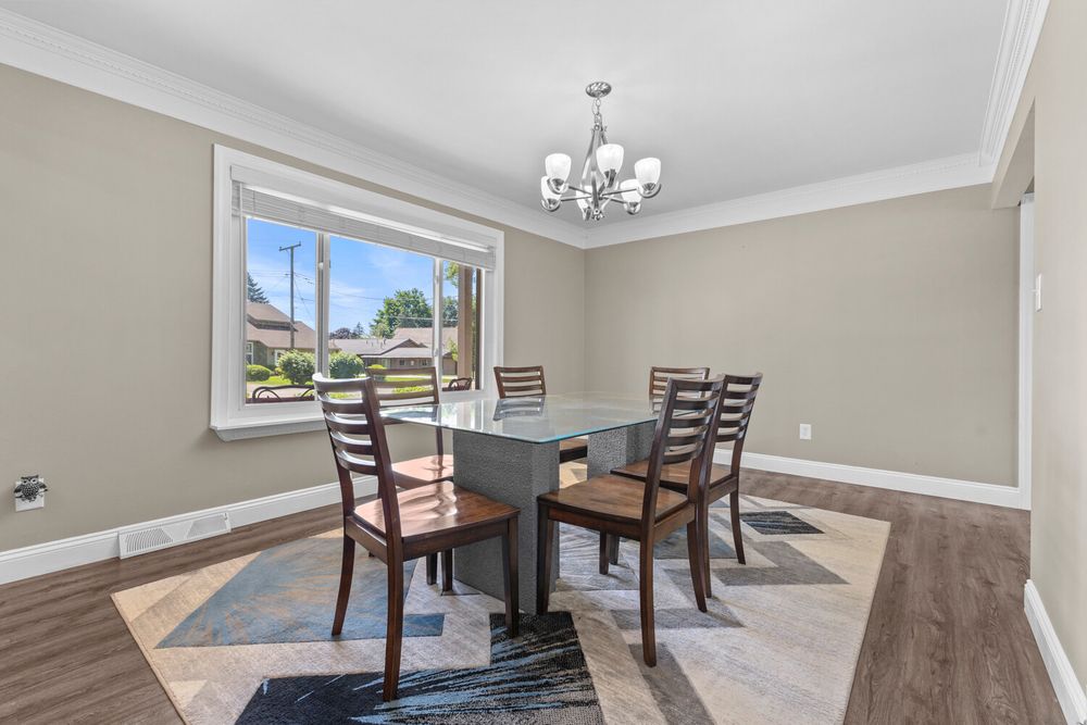 Bright dining room with hardwood floors, crown molding, chandelier, and glass dining table set.
