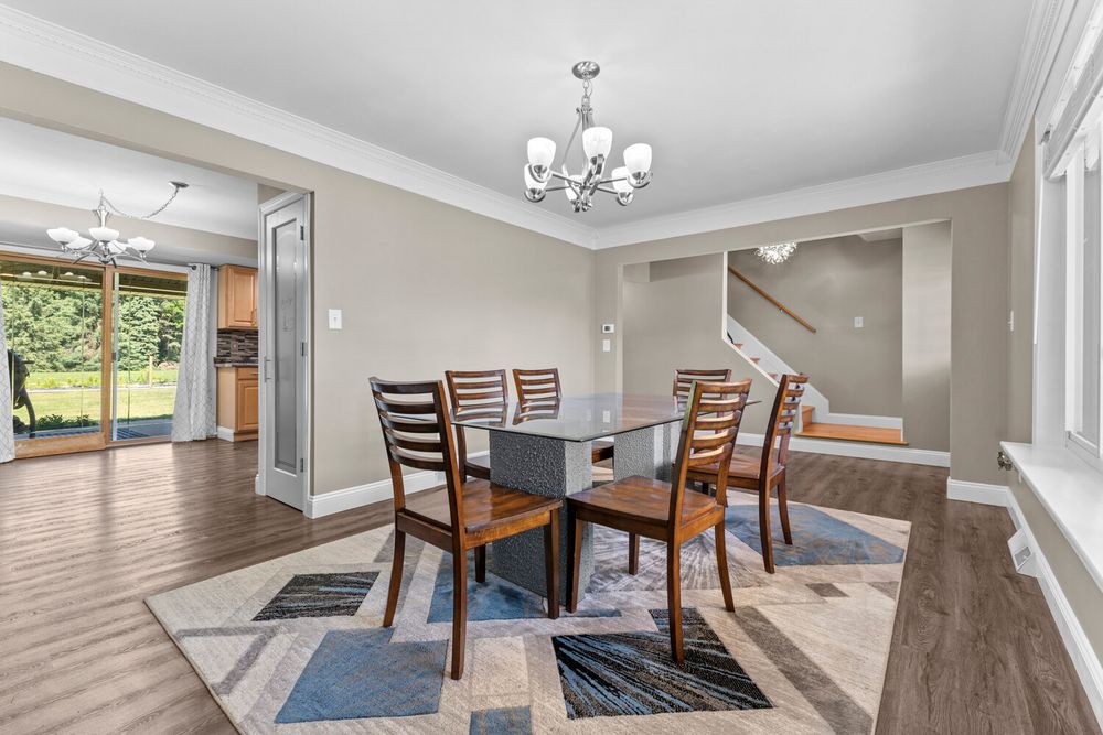 Elegant dining room with dark wood chairs, glass table, geometric area rug, hardwood floors, and chandelier lighting.