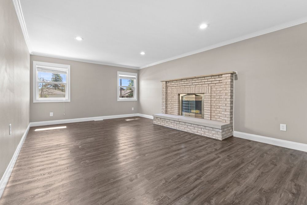 Spacious living room featuring dark hardwood floors, brick fireplace, crown molding, and recessed lighting.