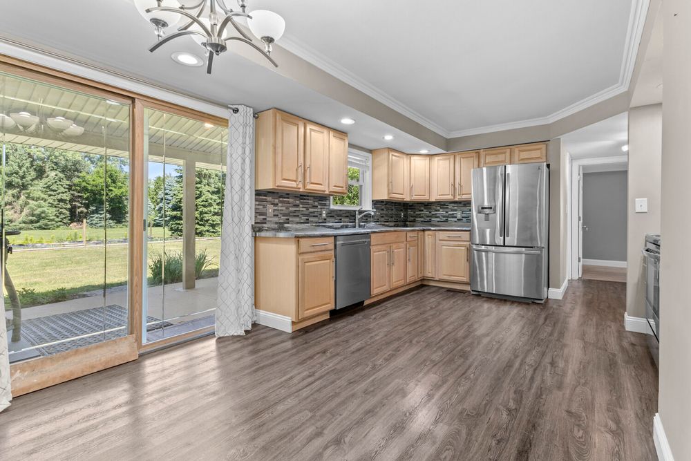 Modern kitchen with light wood cabinets, stainless steel appliances, tile backsplash, and sliding glass door.
