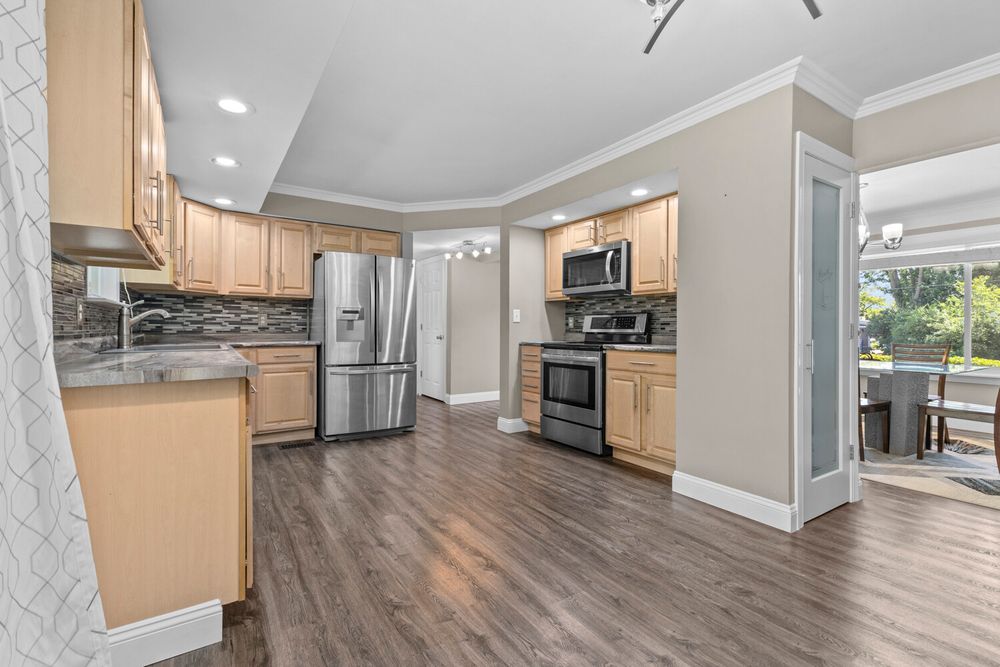 Spacious kitchen with light maple cabinets, stainless appliances, tile backsplash, and dark hardwood floors.