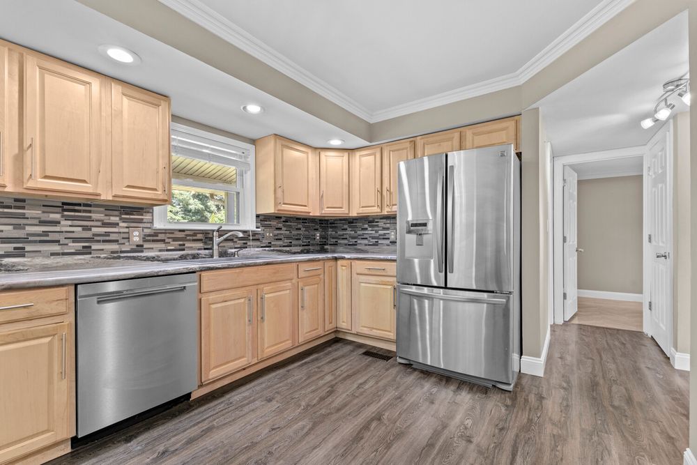 Updated kitchen with light wood cabinetry, stainless steel appliances, stone tile backsplash, and hardwood floors.