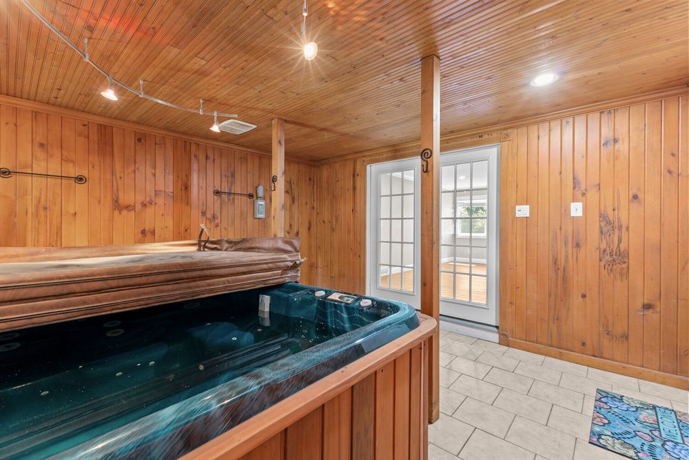 Indoor hot tub room with cedar wood paneling, vaulted ceiling, tile floors, and French doors.