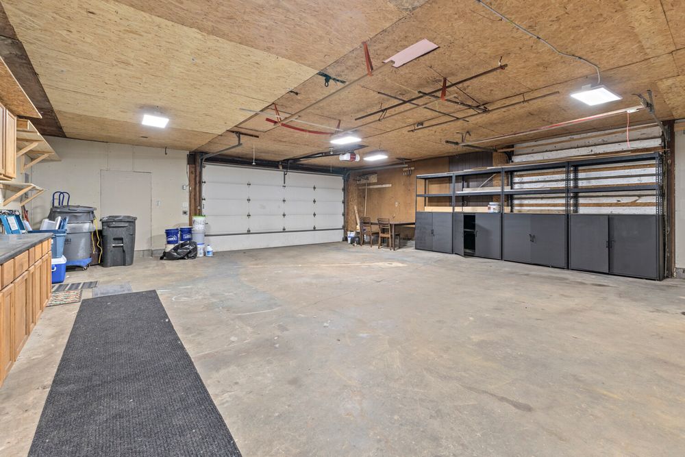 Spacious garage interior with concrete floors, white garage doors, built-in cabinets, and industrial ceiling lighting.