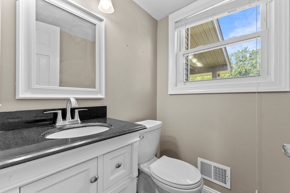 Clean bathroom with white vanity, dark granite countertop, toilet, and natural light from a window.