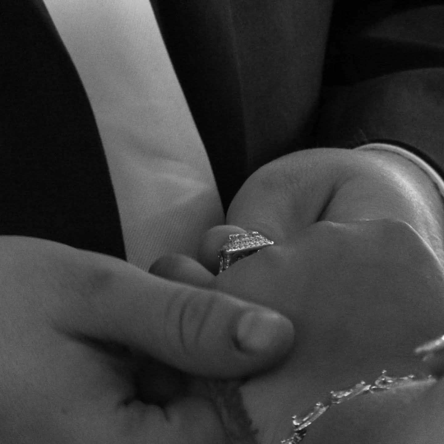 Black and white close-up of couple holding hands with diamond ring at wedding.