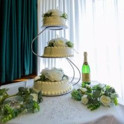 Three-tier white wedding cake on spiral stand with champagne and floral decorations.