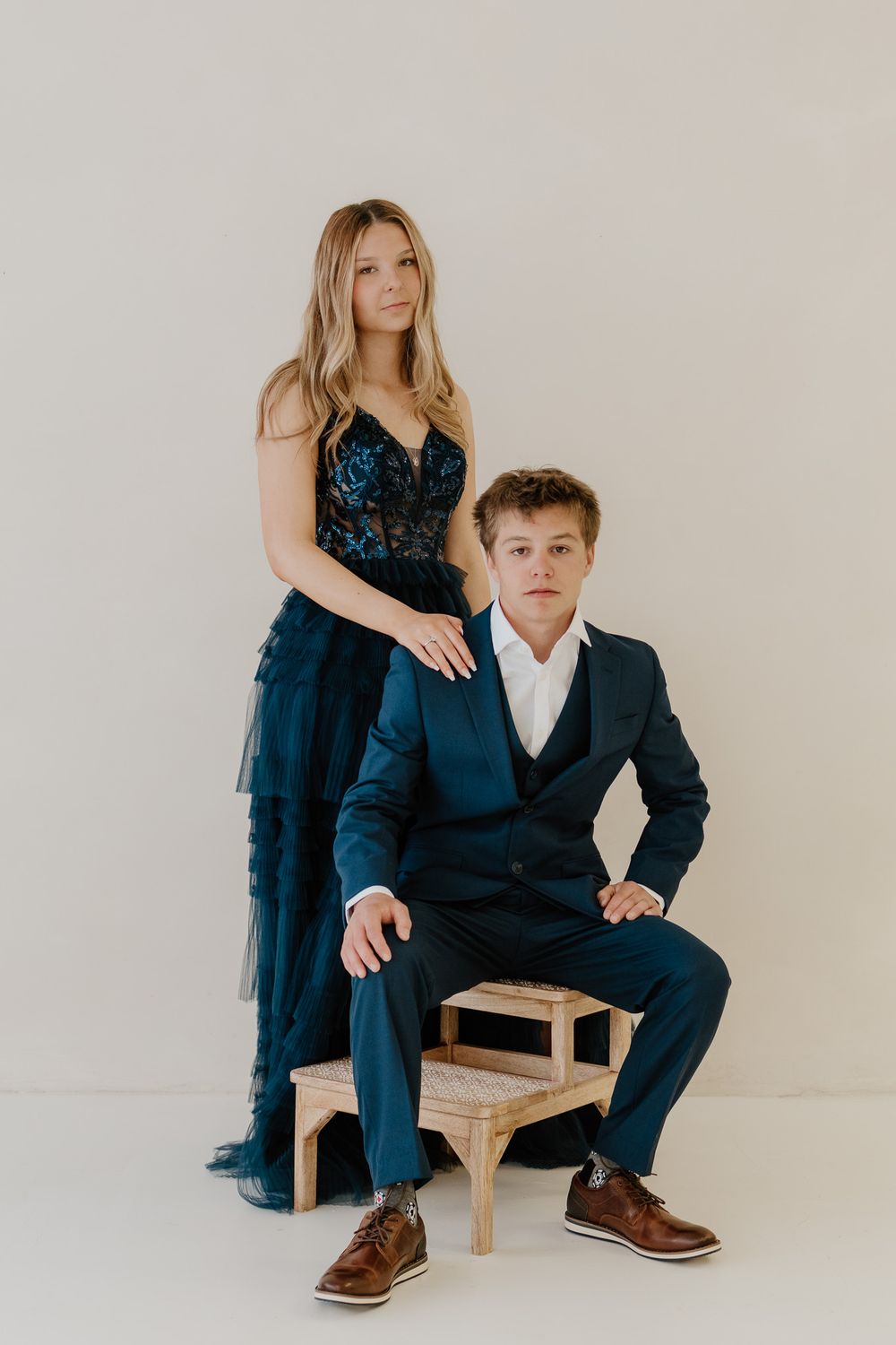 Teen girl in navy blue tulle dress posing with serious boy in blue suit in photo studio.