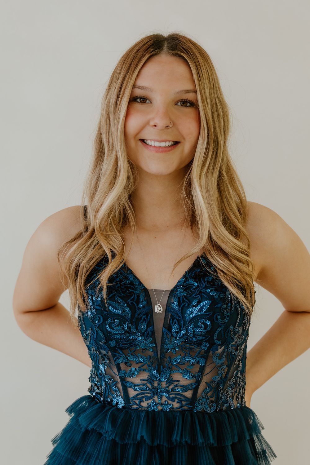 Blonde young woman smiling confidently in teal sequin and tulle formal gown with hands on hips.
