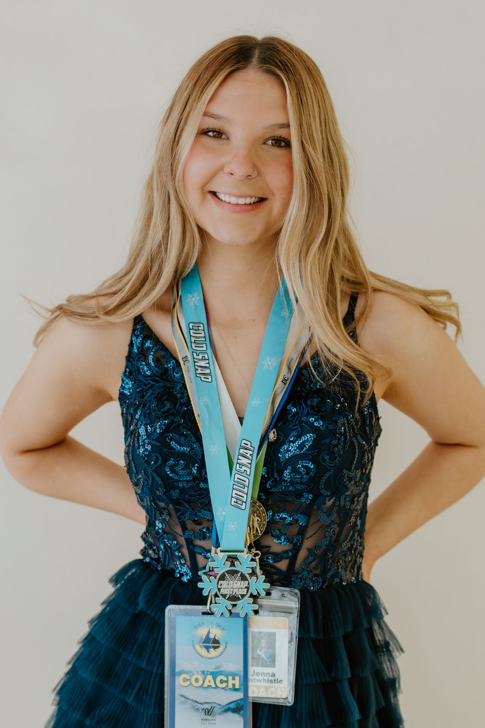 Cheerleading coach in teal sequin gown proudly wearing gold All Star competition medal and badge.