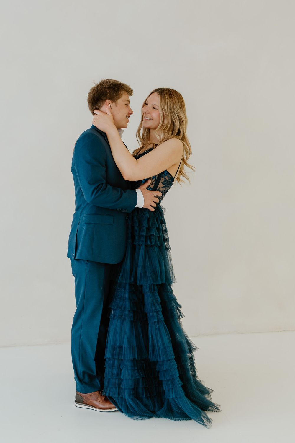 Full-length photo of a young couple in navy blue formal wear sharing a romantic dance pose.