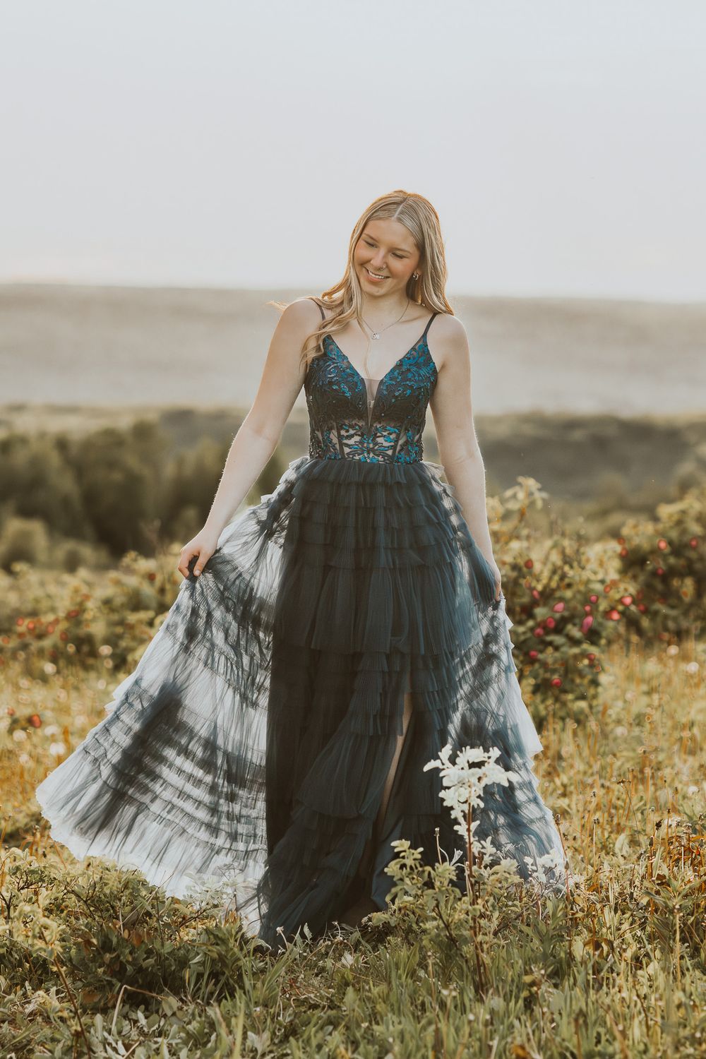 Young blonde woman smiling in a stunning dark teal lace and tulle gown in a meadow.