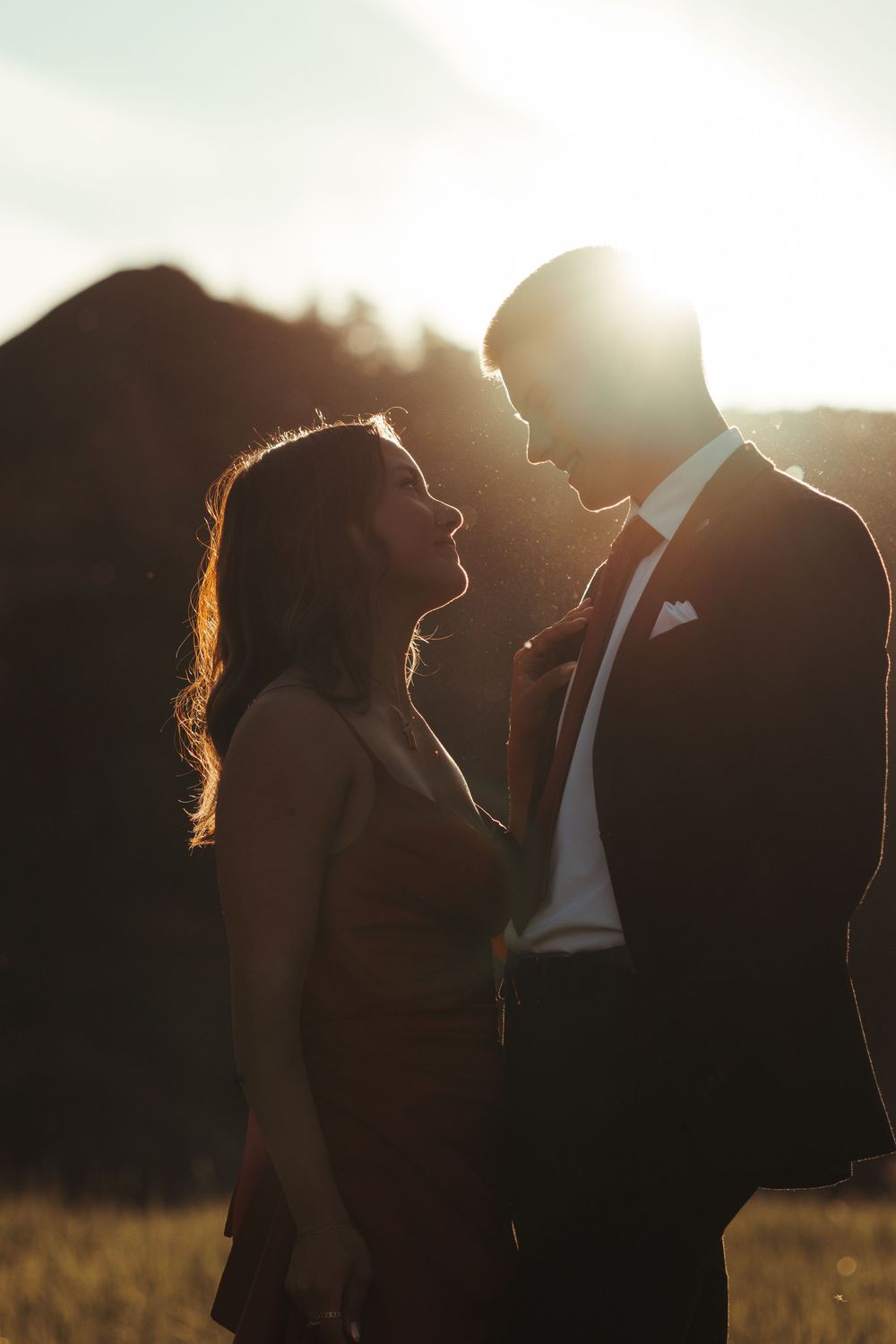 Romantic silhouette of a couple in formal wear facing each other in a glowing sunset field.