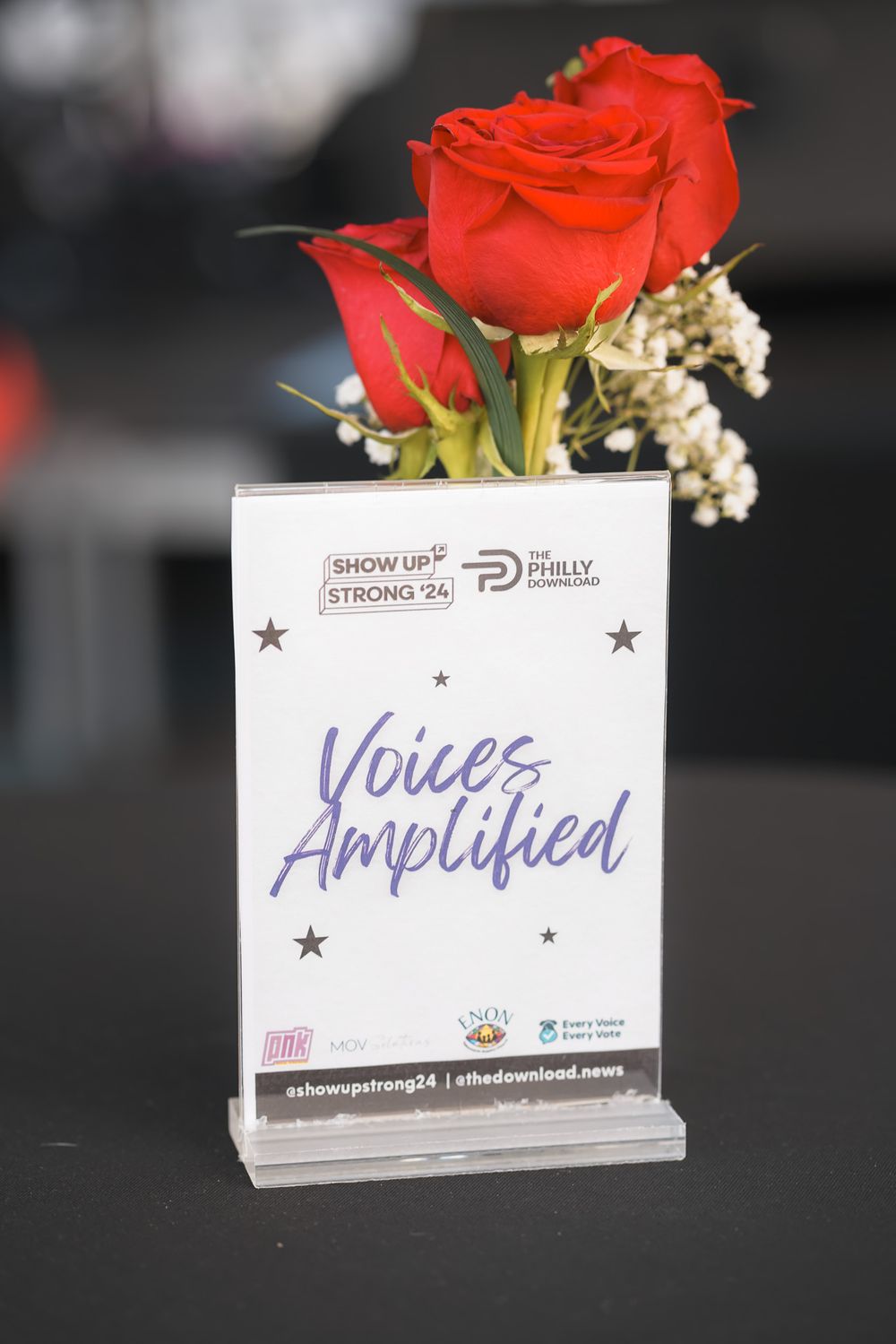 Voices Amplified sign for Show Up Strong 24 and The Philly Download event displayed with red roses.