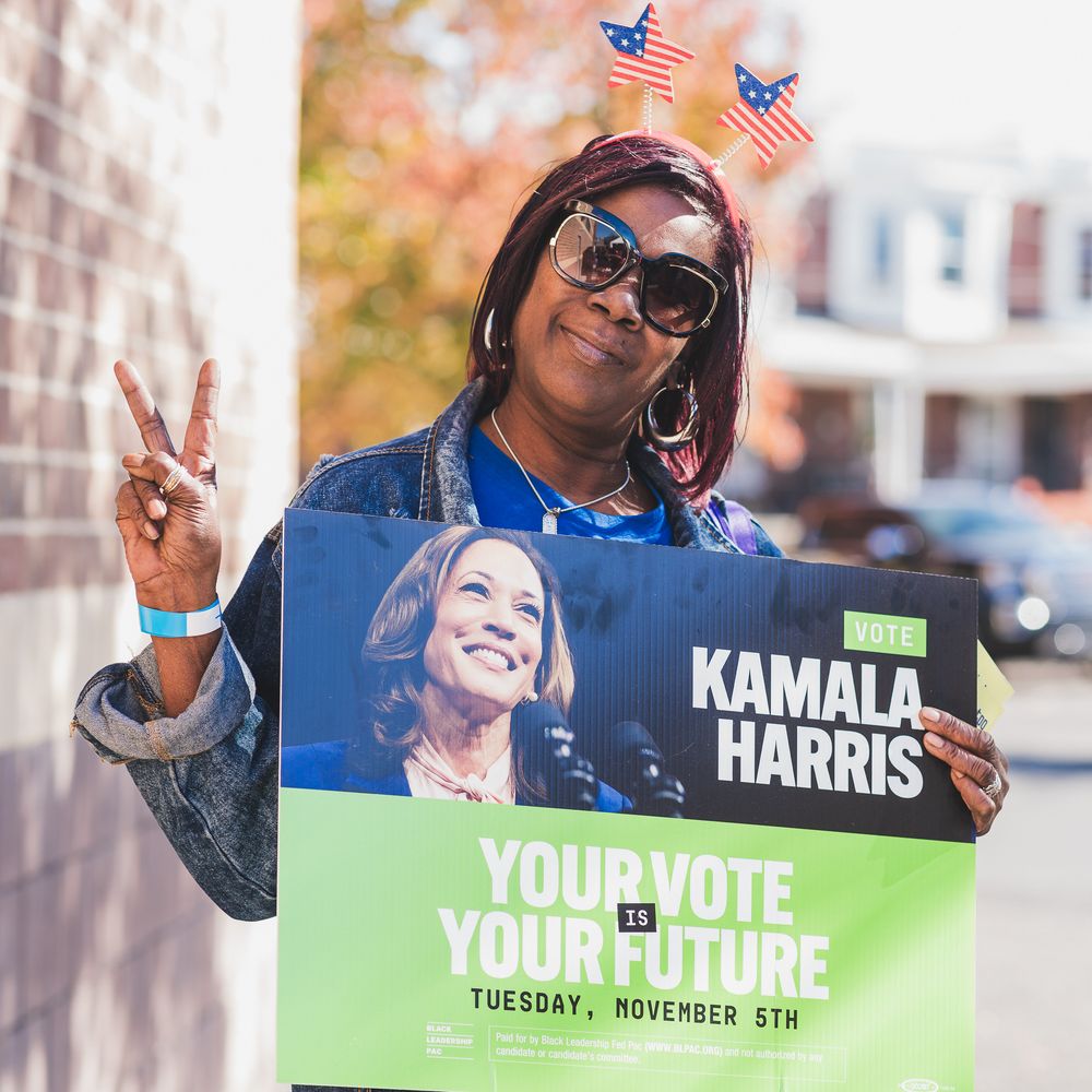Woman wearing American flag headband holds Kamala Harris campaign sign outdoors on Election Day Tuesday November 5th.