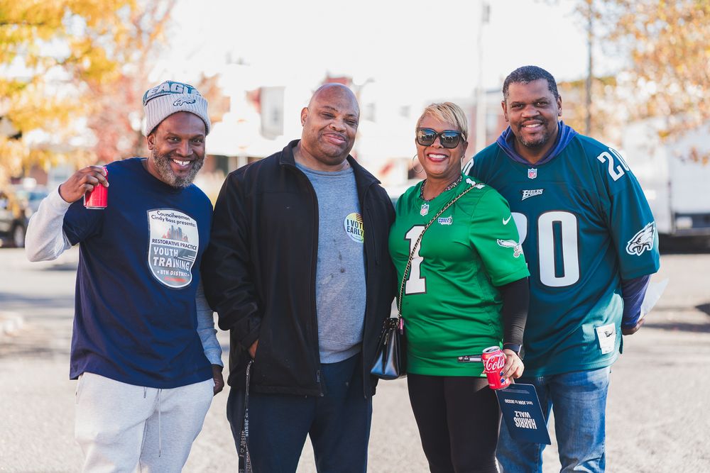 Four friends smile together outdoors wearing Philadelphia Eagles jerseys on a fall day.