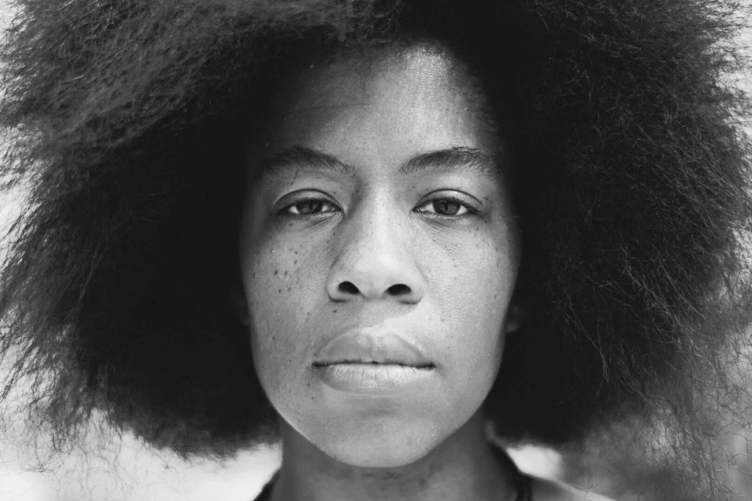 Close-up black and white portrait of a young woman with a large natural afro hairstyle and freckles.
