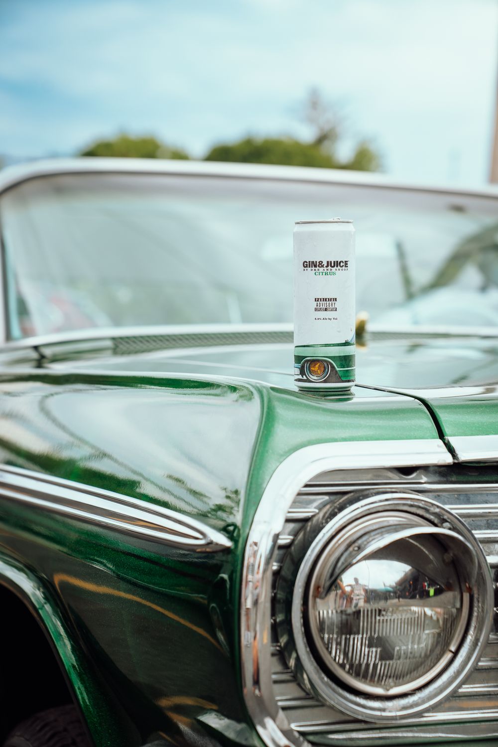A can of Gin & Juice sits on the hood of a shiny green classic car with chrome headlights.