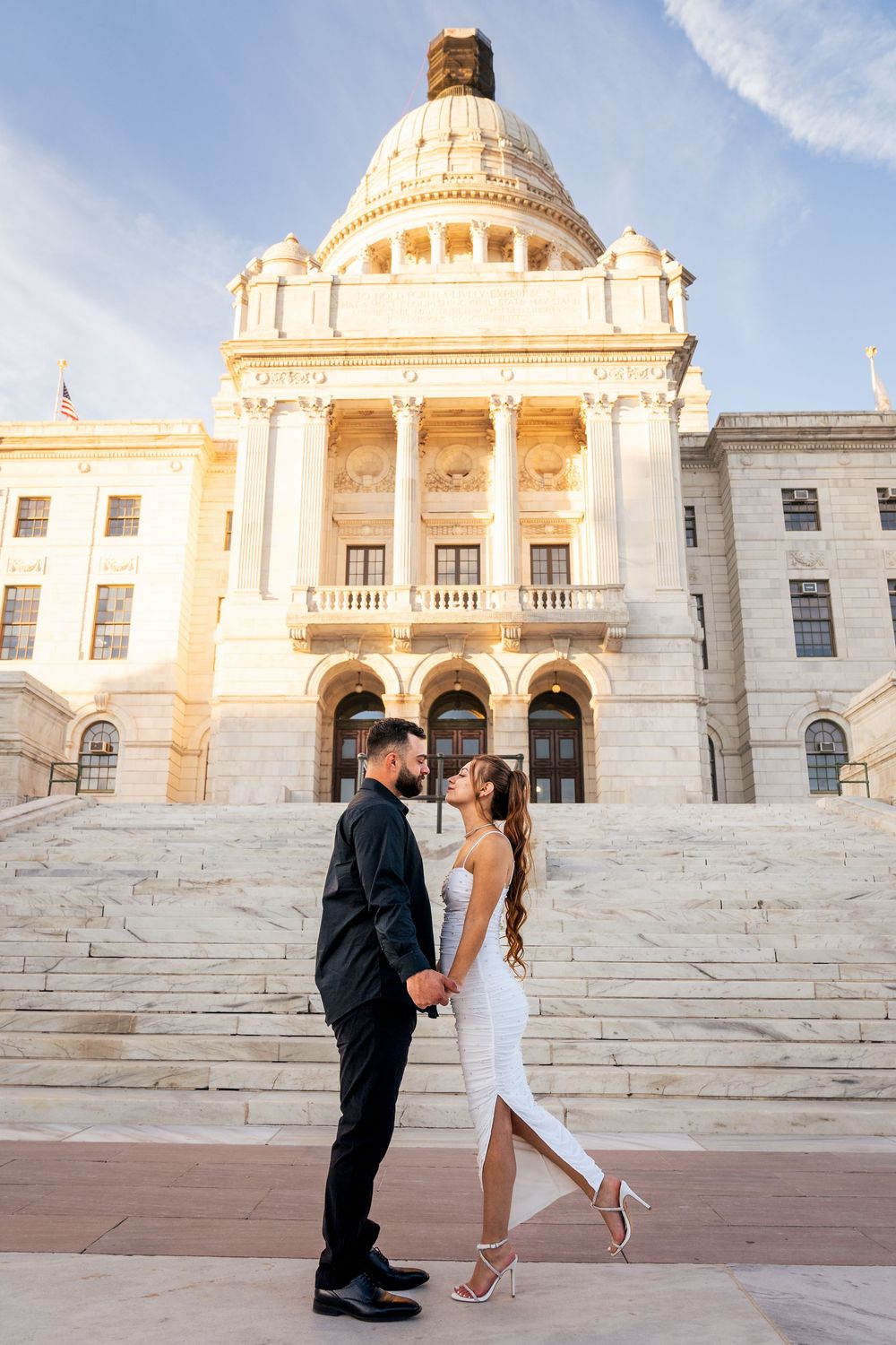 Couple holding hands in formal attire posing in front of a grand capitol building with dome at golden hour.