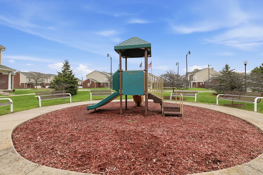 Community playground with green play structure and slide surrounded by wood chip mulch and manicured lawn.
