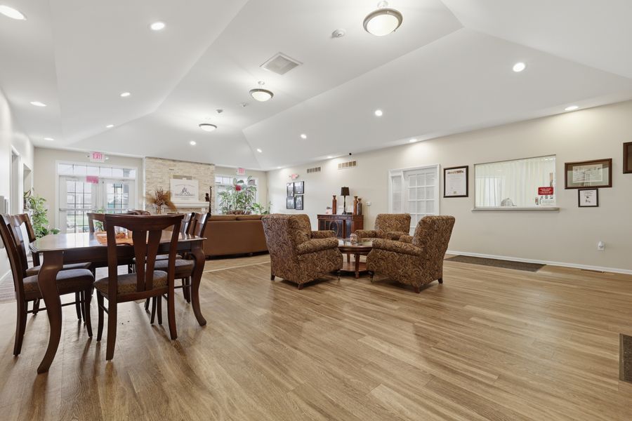 Spacious senior living common area with hardwood floors, dining table, and cozy seating arrangements under vaulted ceilings.