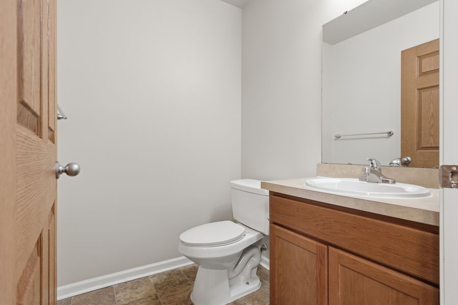 Small bathroom with wood vanity, white toilet, large mirror, and neutral tile flooring in a bright, clean space.