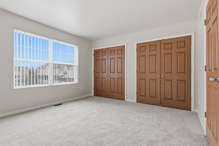 Bright bedroom with carpet, large window, and two wooden closets with six-panel doors.