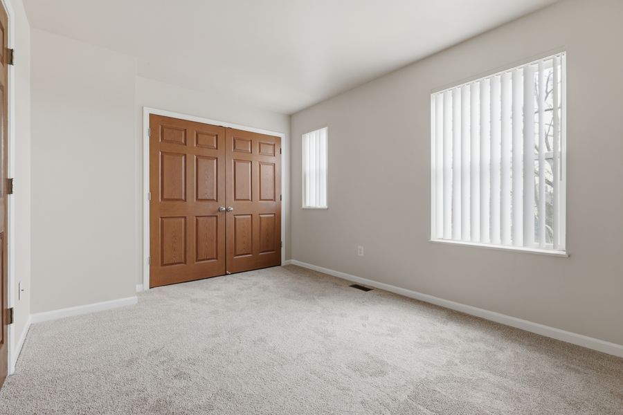 Bright bedroom with plush carpet, double wood closet doors, and large windows with vertical blinds.