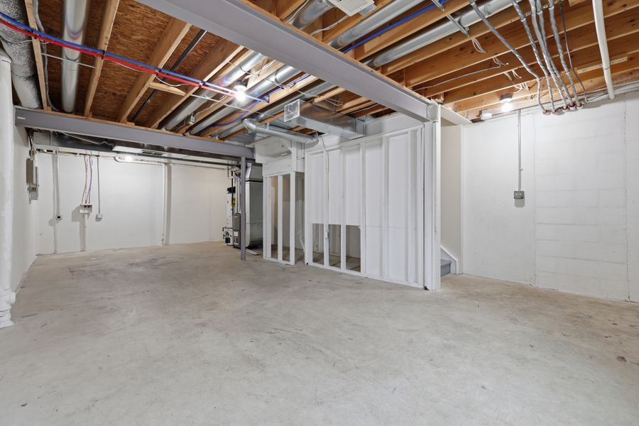 Unfinished basement with white walls, exposed wooden ceiling joists, concrete floors, and utility systems visible.
