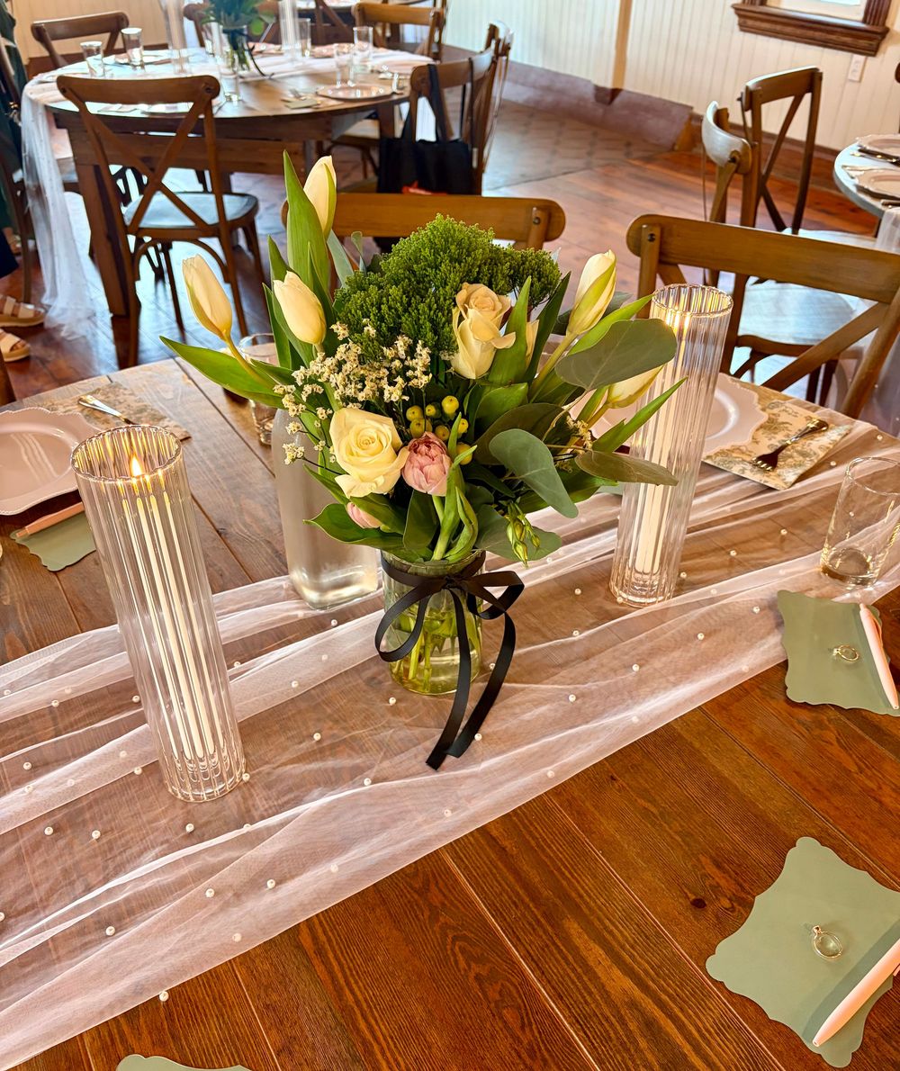 Elegant restaurant table centerpiece with fresh flowers, white tulips, roses, and greenery in a glass vase with candles.