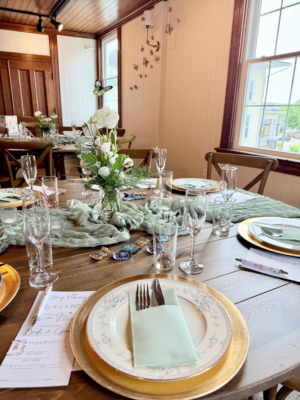 Elegant farmhouse table setting with gold chargers, crystal glasses, sage green napkins, and white floral centerpiece for a formal event.