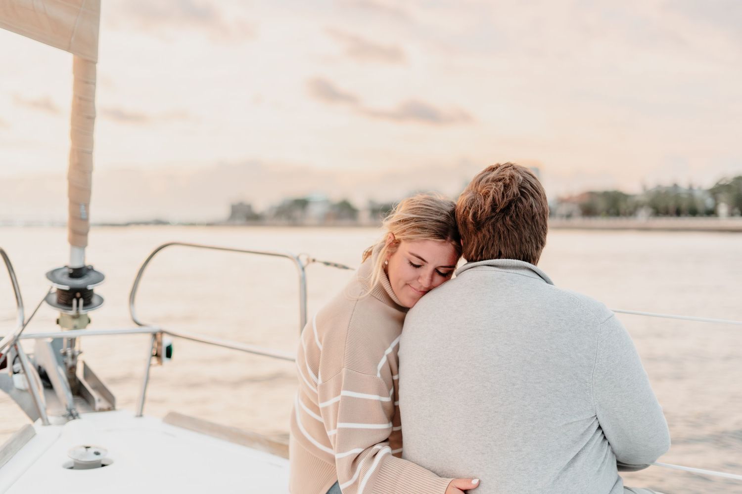 Couple embracing romantically on a sailboat at sunset, woman resting her head on man's shoulder.